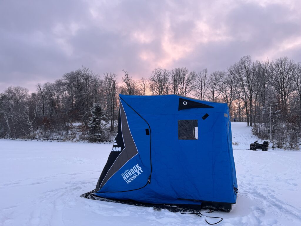 This is a Clam thermal ice portable ice house sitting on a frozen lake. Portable ice houses allow the user to get away from the elements and stay warm while ice fishing.